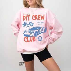 May include: Light pink sweatshirt with a graphic that reads "Mason's Pit Crew Club" in red and blue. The design includes crossed checkered flags, a blue race car, and a steering wheel. The words "start your engines" are also included.