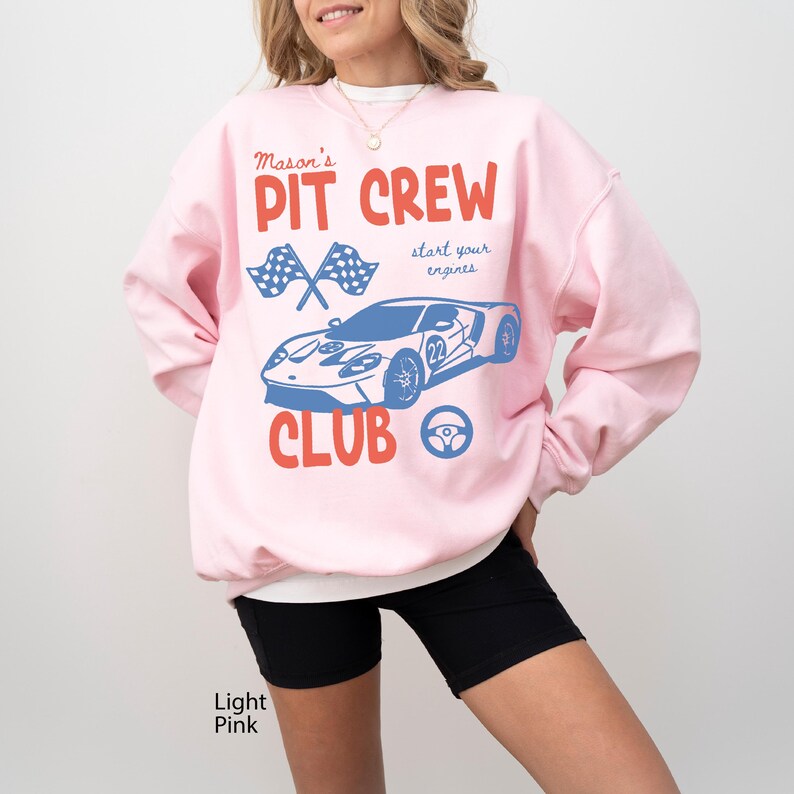 May include: Light pink sweatshirt with a graphic that reads "Mason's Pit Crew Club" in red and blue. The design includes crossed checkered flags, a blue race car, and a steering wheel. The words "start your engines" are also included.