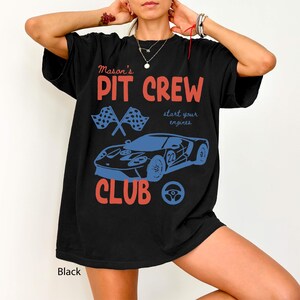May include: Black t-shirt with a racing-themed design. The shirt features the text "Mason's PIT CREW CLUB" in red and blue, along with a blue race car graphic, checkered flags, and a steering wheel.