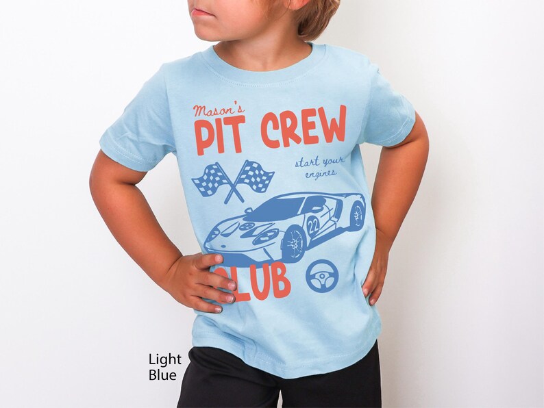 May include: Light blue t-shirt with a car graphic and the words "Mason's Pit Crew Club". The design includes checkered flags, a steering wheel, and the phrase "start your engines".
