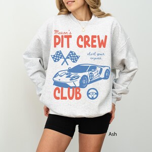 May include: Ash-colored sweatshirt with a racing car graphic. The design includes the words "Mason's Pit Crew Club" in red and blue, along with crossed checkered flags, a steering wheel, and a race car with the number 22.