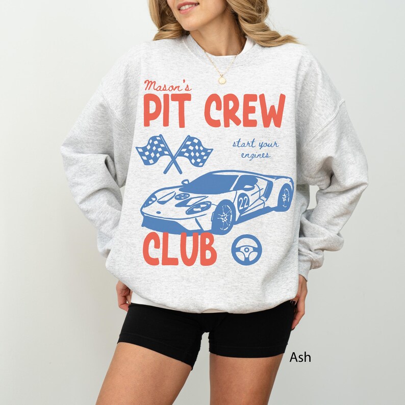 May include: Ash-colored sweatshirt with a racing car graphic. The design includes the words "Mason's Pit Crew Club" in red and blue, along with crossed checkered flags, a steering wheel, and a race car with the number 22.