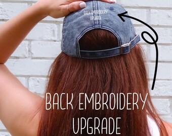 Puede incluir: Gorra de béisbol de mezclilla descolorida con visera curva y correa ajustable. El texto "BACK EMBROIDERY UPGRADE" está bordado en blanco en la parte trasera. La gorra es de color azul descolorido.