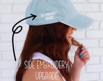 Puede incluir: Gorra de béisbol azul claro con el texto "SIDE EMBROIDERY UPGRADE" en el lateral y en la parte inferior. La gorra tiene una visera curva y la lleva una persona con pelo rojo.