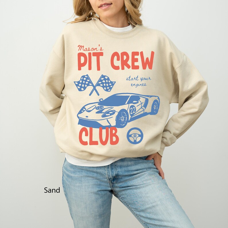 May include: Sand-colored sweatshirt with a red and blue graphic. The design includes the text "Mason's PIT CREW CLUB" with a race car, checkered flags, and a steering wheel. The words "start your engines" are also included.