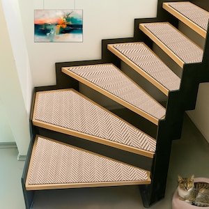 Könnte beinhalten: Treppe mit Stufen mit beigefarbenen und braunen Fischgrätmuster-Treppenstufen. Die Stufen sind auf Holzstufen mit schwarzen Setzstufen angebracht. Ein abstraktes Gemälde hängt an der Wand. Eine Katze ruht auf einem rosa Bett.
