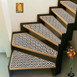 Puede incluir: Escalera con peldaños estampados con un patrón geométrico en blanco y negro. Las huellas están bordeadas por madera clara y colocadas contra contrahuellas negras. Un cuadro enmarcado cuelga de la pared. Un jarrón con flores está al lado.