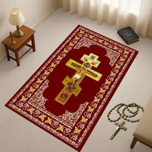 May include: A rectangular red rug with a gold cross design in the centre, featuring an image of Jesus Christ. The rug has a white and gold floral border. A rosary and a book titled "Jesus and the Bible" are next to the rug.