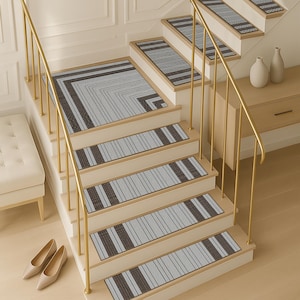 Puede incluir: Un juego de peldaños y una alfombra de aterrizaje de estilo moderno. Los peldaños y la alfombra presentan un patrón de rayas grises y marrones. La escalera tiene una barandilla dorada y está junto a un banco y un mueble pequeño.