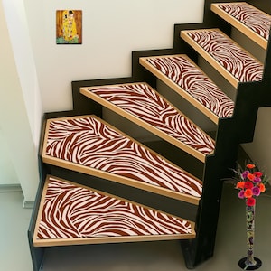 Puede incluir: Escalera con peldaños con estampado de cebra. Los peldaños son marrones y blancos, con un marco negro y un borde de madera clara. Un jarrón de flores de colores y un cuadro enmarcado también son visibles.