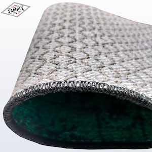 May include: Close-up of a gray, textured rug with a repeating pattern. The edge is finished with black stitching. The underside is a dark green color. A small diamond-shaped graphic with the word "SAMPLE" is in the upper left corner.