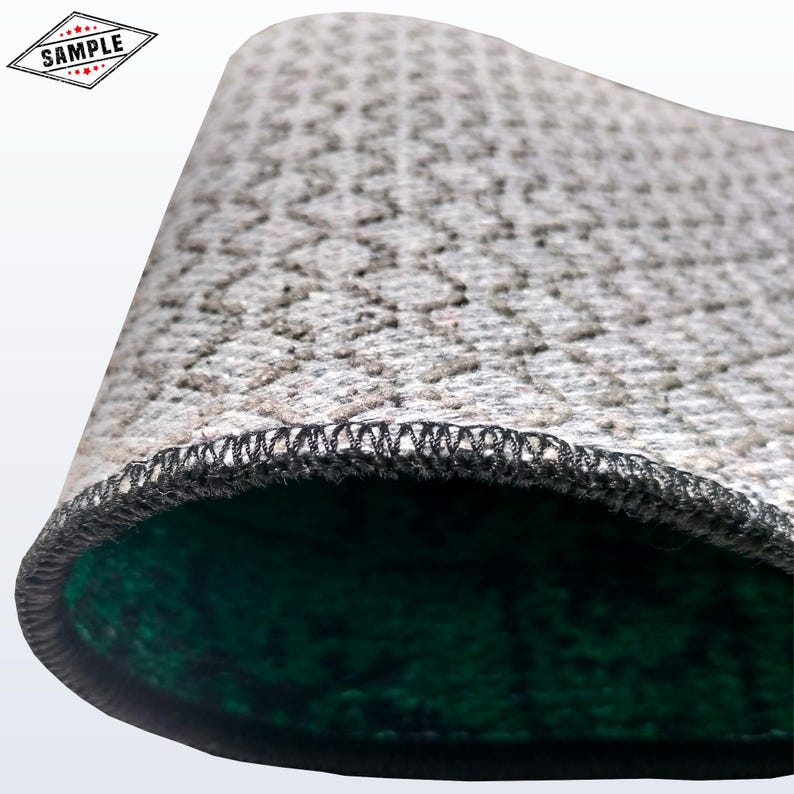 May include: Close-up of a gray, textured rug with a repeating pattern. The edge is finished with black stitching. The underside is a dark green color. A small diamond-shaped graphic with the word "SAMPLE" is in the upper left corner.