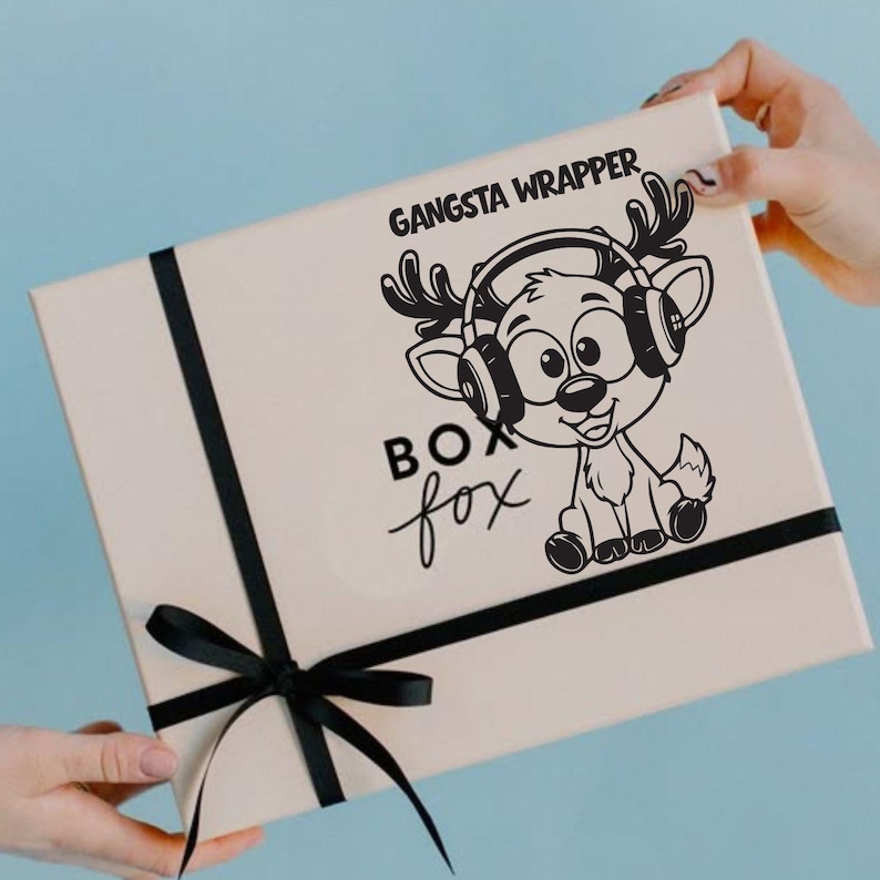 Op de afbeelding: Een beige geschenkdoos met een zwart lint en strik. De doos heeft een cartoonvos met een koptelefoon en de tekst "Gangsta Wrapper" en "Box Fox" in het zwart.