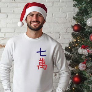 May include: A white sweatshirt with blue and red Japanese characters. The person in the image is wearing a red and white Santa hat. A Christmas tree with ornaments is in the background.