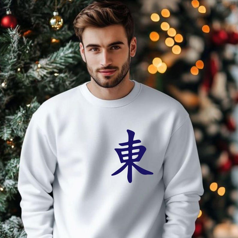 May include: A white sweatshirt with a dark blue Japanese character on the front. The sweatshirt is made of a soft material and has a crew neck. The background includes a Christmas tree with ornaments and lights.