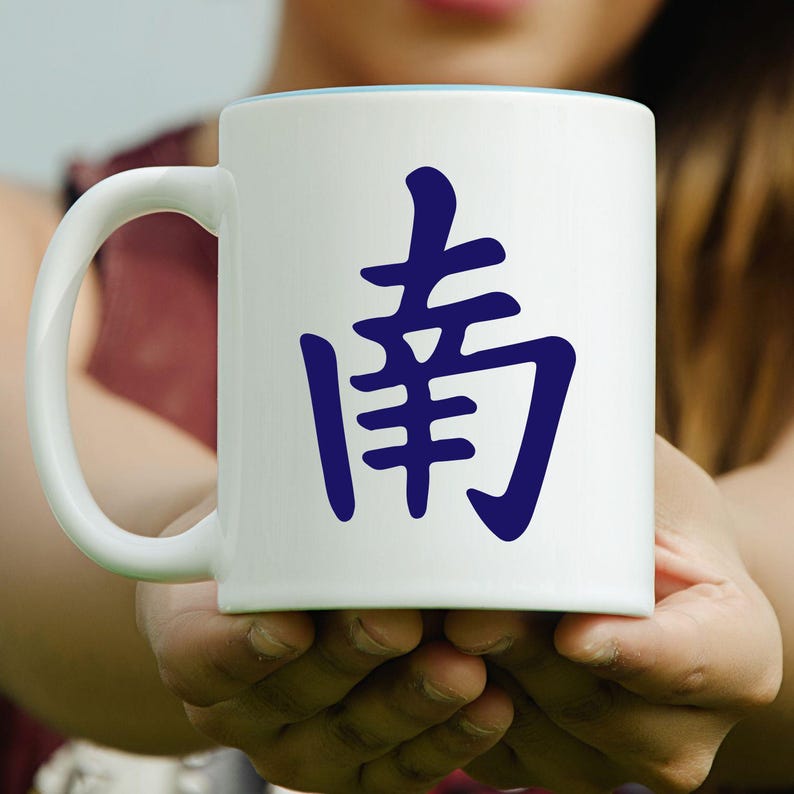 May include: White ceramic mug with a blue interior rim and a large blue Chinese character on the front. The mug has a curved handle and is held in both hands.