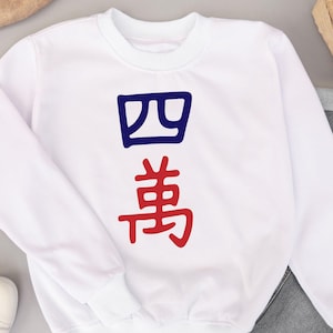 May include: White crewneck sweatshirt with the Chinese characters for "four ten thousand" in blue and red. The characters are vertically aligned on the front of the sweatshirt. The sweatshirt is made of a soft material.
