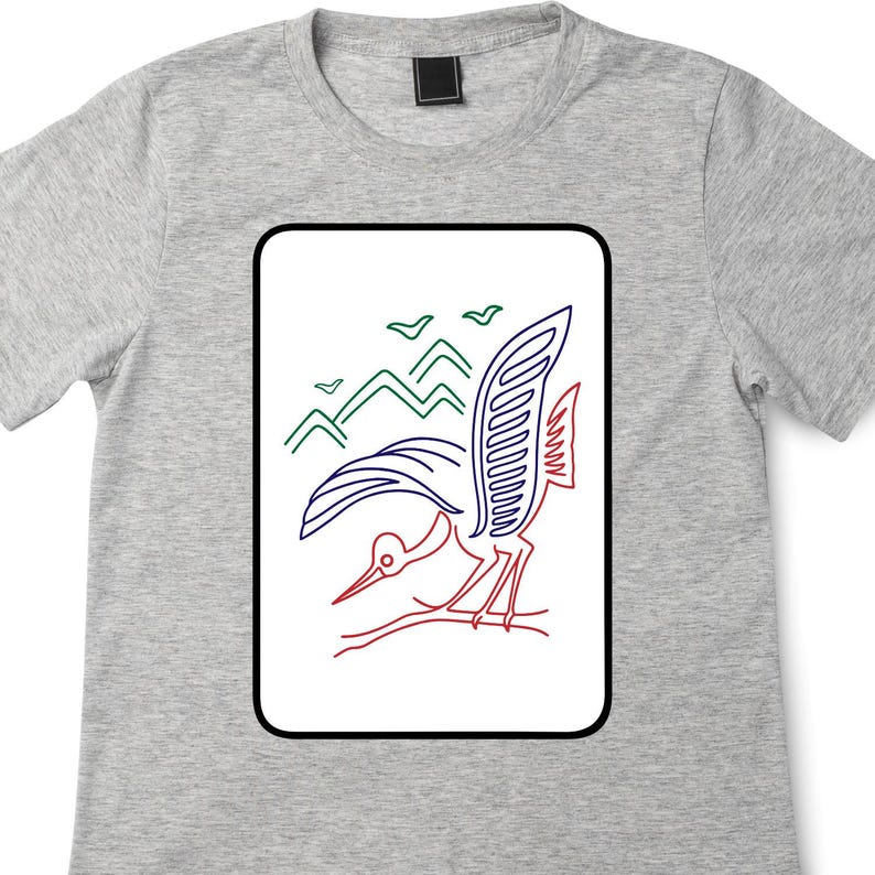 May include: A light gray t-shirt featuring a rectangular graphic with a bird design. The bird is depicted with red, blue, and white outlines, with green mountains and birds in the background. The shirt has a crew neck.