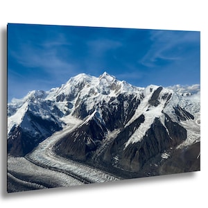 May include: A scenic photograph of a snow-covered mountain range under a clear blue sky. The mountain peaks are covered in white snow, with glaciers visible in the valleys. The sky is a vibrant blue with wispy clouds.
