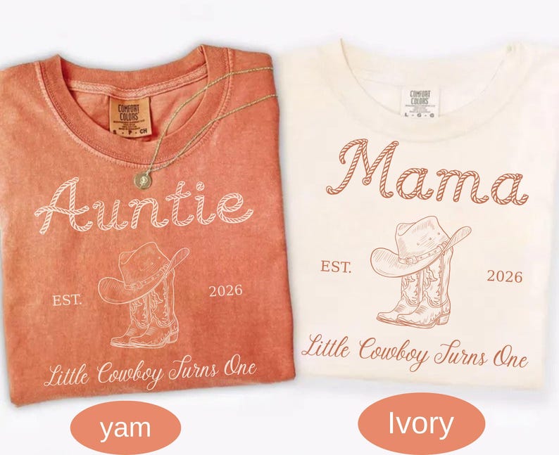 May include: Two crew neck t-shirts in yam and ivory colors. The yam shirt features white text reading Auntie, a cowboy hat and boot graphic, and Little Cowboy Turns One. The ivory shirt features brown text reading Mama, the same graphic, and Little Cowboy Turns One.
