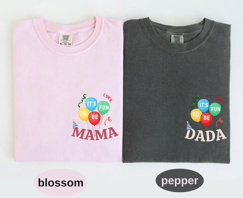 Pu&ograve; includere: Una t-shirt rosa chiaro e una t-shirt grigio scuro, ciascuna con una grafica di palloncini colorati con il testo IT'S FUN TO BE MAMA sulla maglietta rosa e IT'S FUN TO BE DADA su quella grigia, accompagnate da cappellini e festoni.
