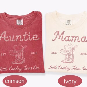 May include: Two short-sleeve t-shirts in crimson and ivory. The crimson shirt features white text reading Auntie, EST. 2026, and Little Cowboy Turns One with a cowboy hat and boots graphic. The ivory shirt features matching maroon text and graphics.