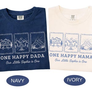 Pu&ograve; includere: Due magliette, una blu navy e una color avorio, con disegni a tema campeggio abbinati. Ognuna presenta tre illustrazioni incorniciate e il testo "ONE HAPPY DADA" o "ONE HAPPY MAMA". &Egrave; presente anche il testo "Our Little Sophia is One".