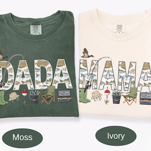 May include: Two short-sleeve t-shirts in moss green and ivory. The moss shirt features the text DADA and the ivory shirt features MAMA, both filled with fish illustrations. Graphics include a fishing rod, duck, boots, hat, bobber, bucket, chair, and tackle box.