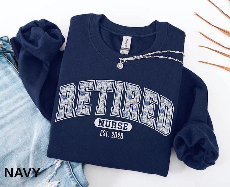 Navy-colored sweatshirt featuring floral varsity ‘RETIRED’ text with ‘NURSE’ and ‘EST. 2026’ printed underneath.