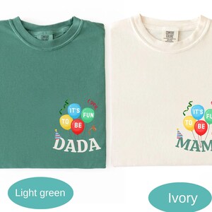 Pu&ograve; includere: Una t-shirt verde chiaro e una t-shirt color avorio, entrambe con una grafica di palloncini colorati con il testo IT'S FUN TO BE DADA sulla maglia verde e IT'S FUN TO BE MAMA su quella avorio, con stelle filanti e un piccolo cappellino.