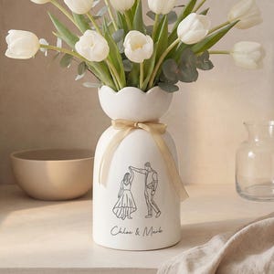 May include: A white ceramic mug with a black handle and the text "But First, Coffee" in a black, handwritten-style font. The mug is on a white surface.