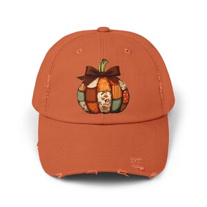 Op de afbeelding: Oranje baseballpet met een gerafelde rand. De pet heeft een kleurrijk pompoenontwerp met een bruine strik. De pompoen is gemaakt van patchworkstof met bloemen- en bladerpatronen, perfect voor de herfst.