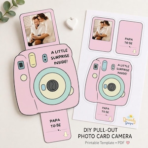 May include: A pink DIY pull-out photo card camera template featuring a light blue lens, a pull-out tab with the text 'PAPA TO BE', and a top section displaying a photograph of a couple. The text 'A LITTLE SURPRISE INSIDE!' is printed on the camera.