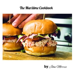 May include: Two lobster rolls on white buns with lettuce and tomato, on a wooden cutting board. The Maritime Cookbook by John Morris.
