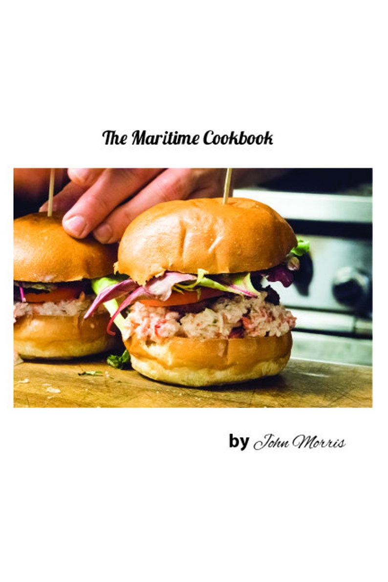 May include: Two lobster rolls on white buns with lettuce and tomato, on a wooden cutting board. The Maritime Cookbook by John Morris.