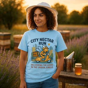May include: A light blue t-shirt with the text "CITY NECTAR RUN" and a cartoon bee riding a scooter. The graphic includes the words "DELIVERING THE GOODS IN THE URBAN JUNGLE". The person is wearing a white hat.