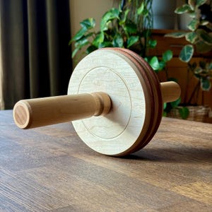 Può includere: Un mattarello in legno con finitura in legno chiaro. Il mattarello presenta un design circolare con un manico centrale in legno e una fascia marrone-rossastra a contrasto sul bordo. Progettato per l'uso in cucina.