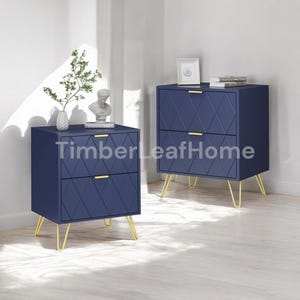 May include: Two navy blue nightstands with gold hairpin legs. Each nightstand has two drawers with gold handles and a diamond pattern on the front. The text "Timber Leaf Home" is visible on the front of the nightstands.