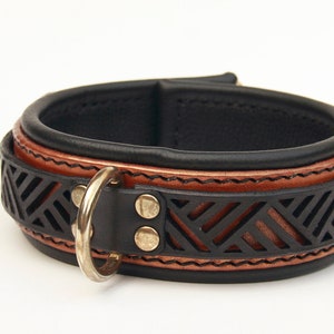 May include: A black leather dog collar with a brown leather trim and a geometric pattern. The collar has a silver D-ring and two brass studs.