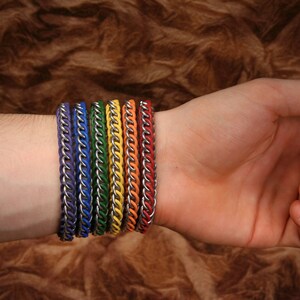 Pode incluir: Um conjunto de seis pulseiras de malha met&aacute;lica com elos prateados alternados com cord&otilde;es de cores vibrantes em roxo, azul, verde, amarelo, laranja e vermelho. Cada pulseira &eacute; constru&iacute;da com um padr&atilde;o repetitivo de segmentos met&aacute;licos.
