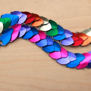 May include: A rainbow colored chainmail bracelet with silver clasps. The bracelet is made of small, heart-shaped metal pieces.