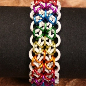 Pode incluir: Um bracelete de malha de corrente arco-íris com elos brancos. O bracelete é feito de metal e tem um design tecido.