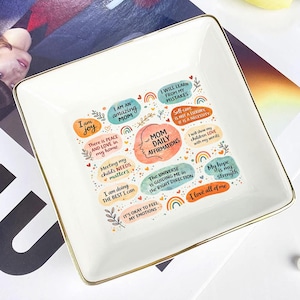 Könnte beinhalten: Eine weiße Keramik-Tasse mit schwarzem Henkel und dem Text "But First, Coffee" in schwarzer, fetter Schrift. Die Tasse steht auf einer Holzoberfläche. Die Tasse ist etwa 10 cm hoch.