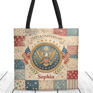 Puede incluir: Bolso tote con diseño de patchwork. Presenta un emblema con un águila, banderas y el texto "250th Anniversary". El bolso tiene asas negras y el nombre "Sophia" debajo del emblema. El fondo es una mezcla de patrones florales y a rayas.