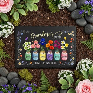 Pode incluir: Uma placa de jardim retangular preta com as palavras "Grandma's Garden" em escrita dourada. Apresenta seis frascos cheios de flores coloridas, cada um com um nome. A frase "Love Grows Here" está abaixo dos frascos. A placa é rodeada por flores e vegetação.