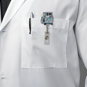 May include: A medical-themed badge reel featuring a cartoon ventilator design in blue, yellow, and white. The badge reel is attached to a white lab coat pocket with a pen. The reel has a clear plastic strap and a metal clip.