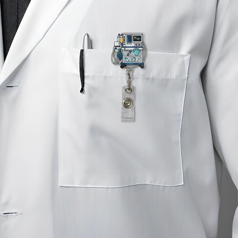 May include: A medical-themed badge reel featuring a cartoon ventilator design in blue, yellow, and white. The badge reel is attached to a white lab coat pocket with a pen. The reel has a clear plastic strap and a metal clip.