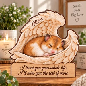 Peut inclure: Une plaque commémorative en bois avec un cadre en ailes d'ange sculptées entourant un hamster endormi. Le nom Oliver est gravé sur l'aile supérieure et la base porte le texte : I loved you your whole life, I'll miss you the rest of mine.