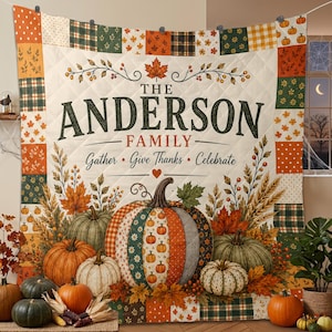 May include: A quilted throw blanket featuring a patchwork border of autumn-themed patterns. The center displays the text THE ANDERSON FAMILY, Gather, Give Thanks, Celebrate, and a large central pumpkin surrounded by wheat and fall leaves.