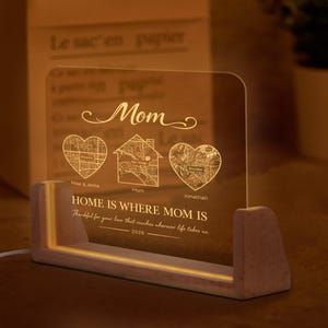 May include: A personalised LED night light with a wooden base. The clear acrylic panel displays the word "Mom" and three map designs within hearts and a house. Text reads "HOME IS WHERE MOM IS" and "Thankful for your love..." with the year 2026.